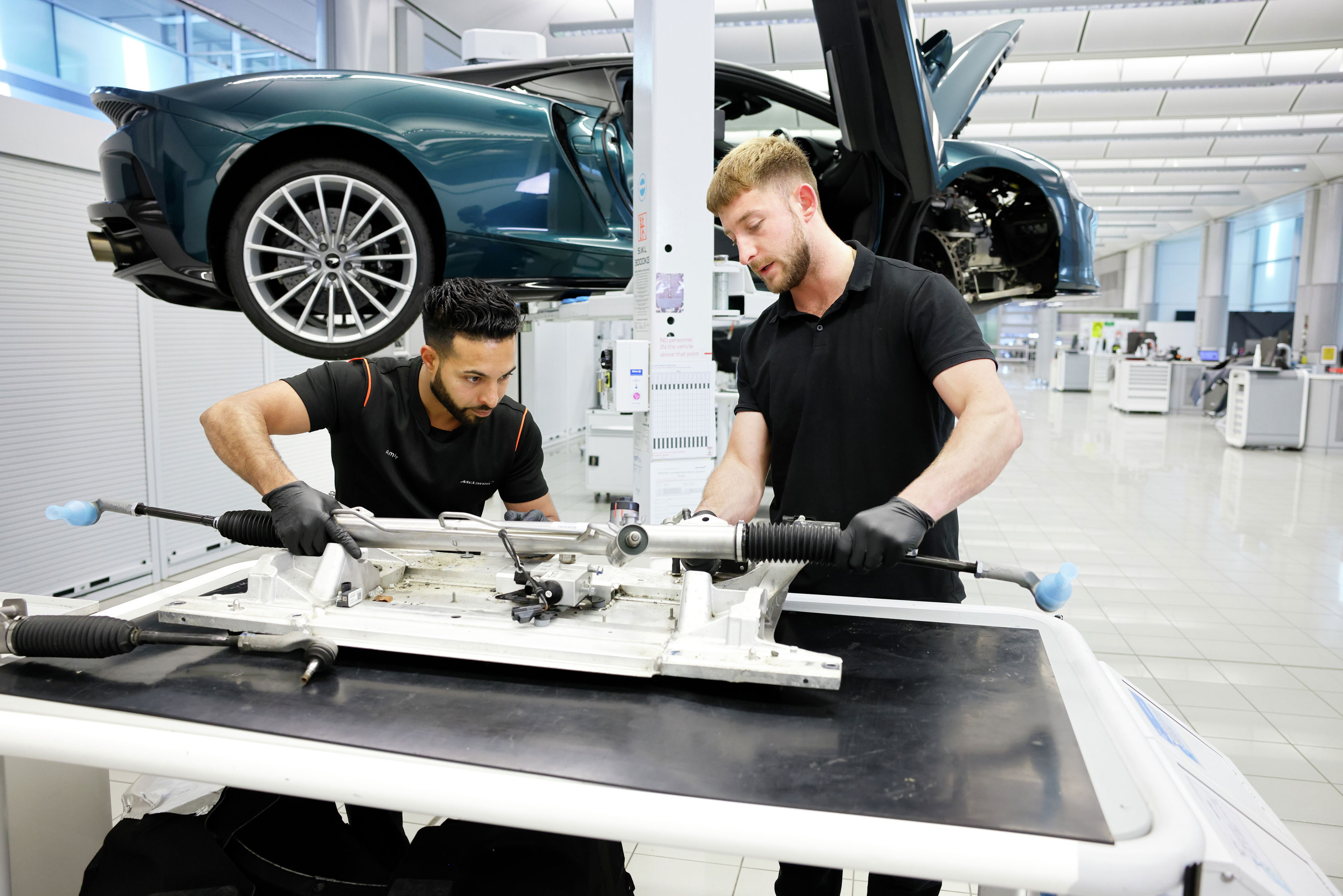 Two McLaren employees are working together on a car component on a workbench.