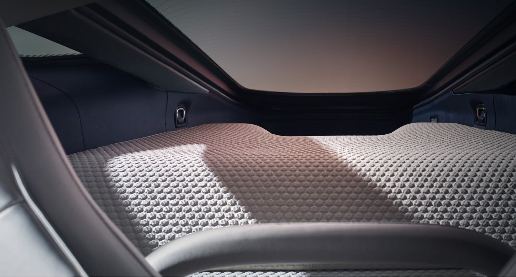 A close-up of the rear luggage area of a McLaren GT, showing the premium, finely woven material with a textured pattern and the open sky visible through the rear glass roof.