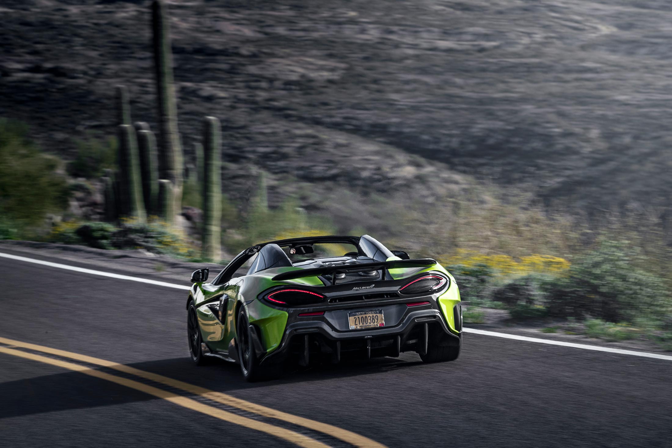  A rear-view action shot of a vibrant lime green McLaren 600LT driving on a winding desert road with cactuses in the background.