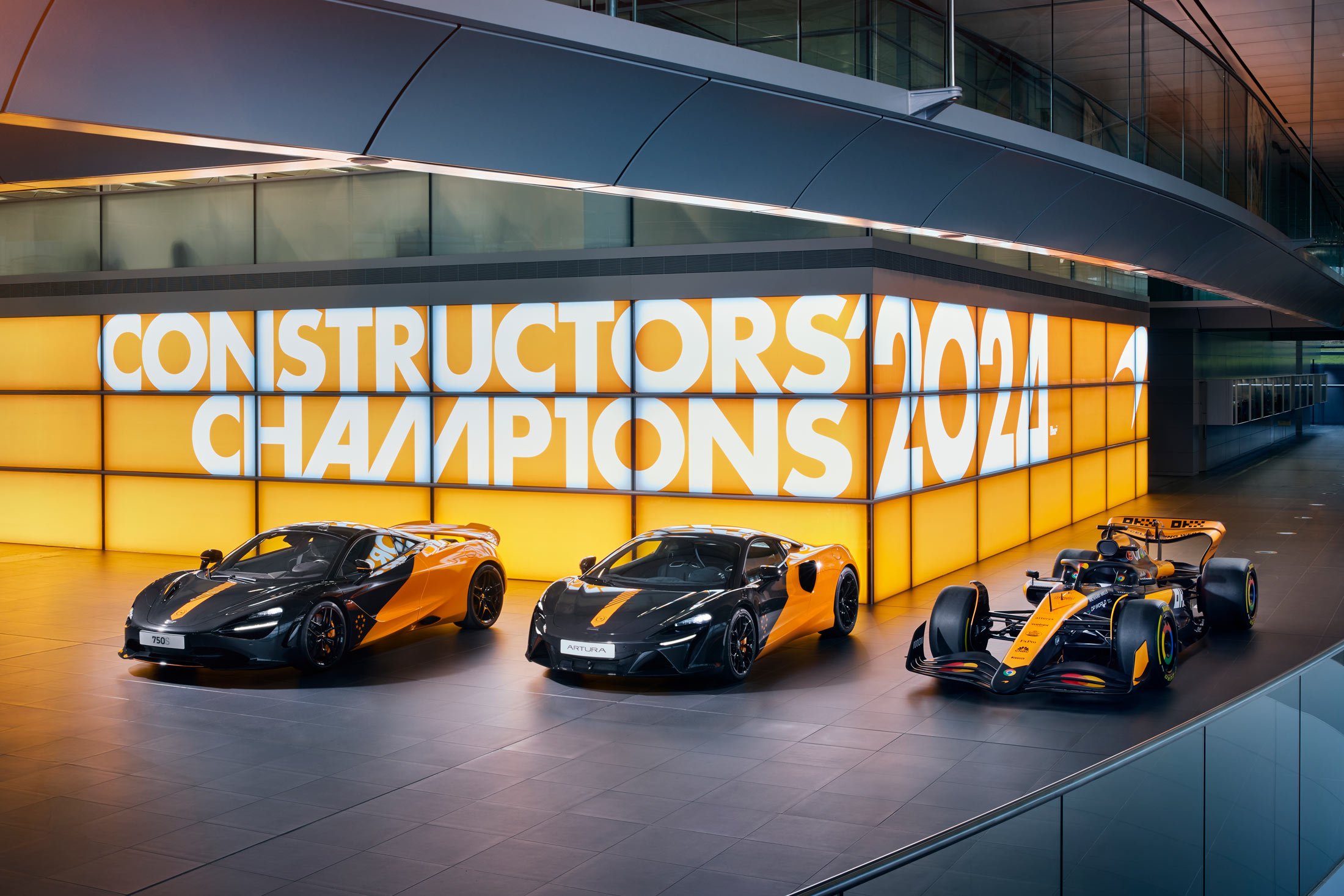 1: A lineup of three McLaren vehicles—a 750S, an Artura, and a Formula 1 car—all in a matching orange and black livery, celebrating the brand's racing heritage.