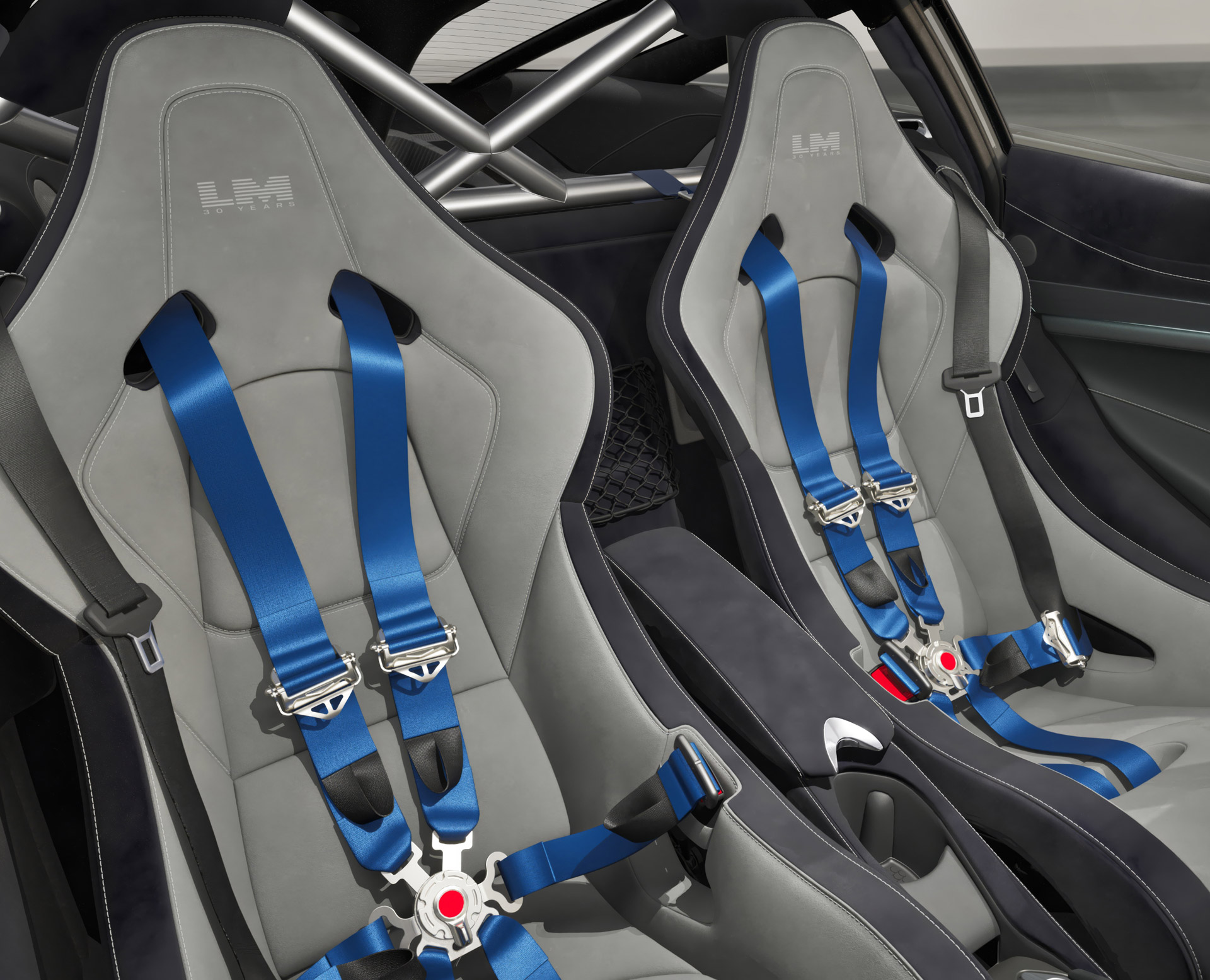 A close-up of the grey carbon fiber racing seats with blue six-point harnesses and embroidered 'LM' logos in the McLaren 750S Le Mans.