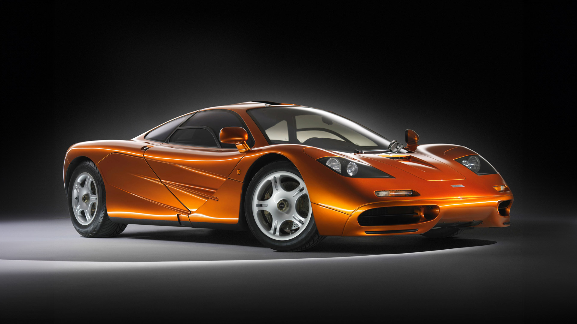 The iconic McLaren F1, the legendary hypercar, finished in a signature McLaren Orange paint, in a studio setting.