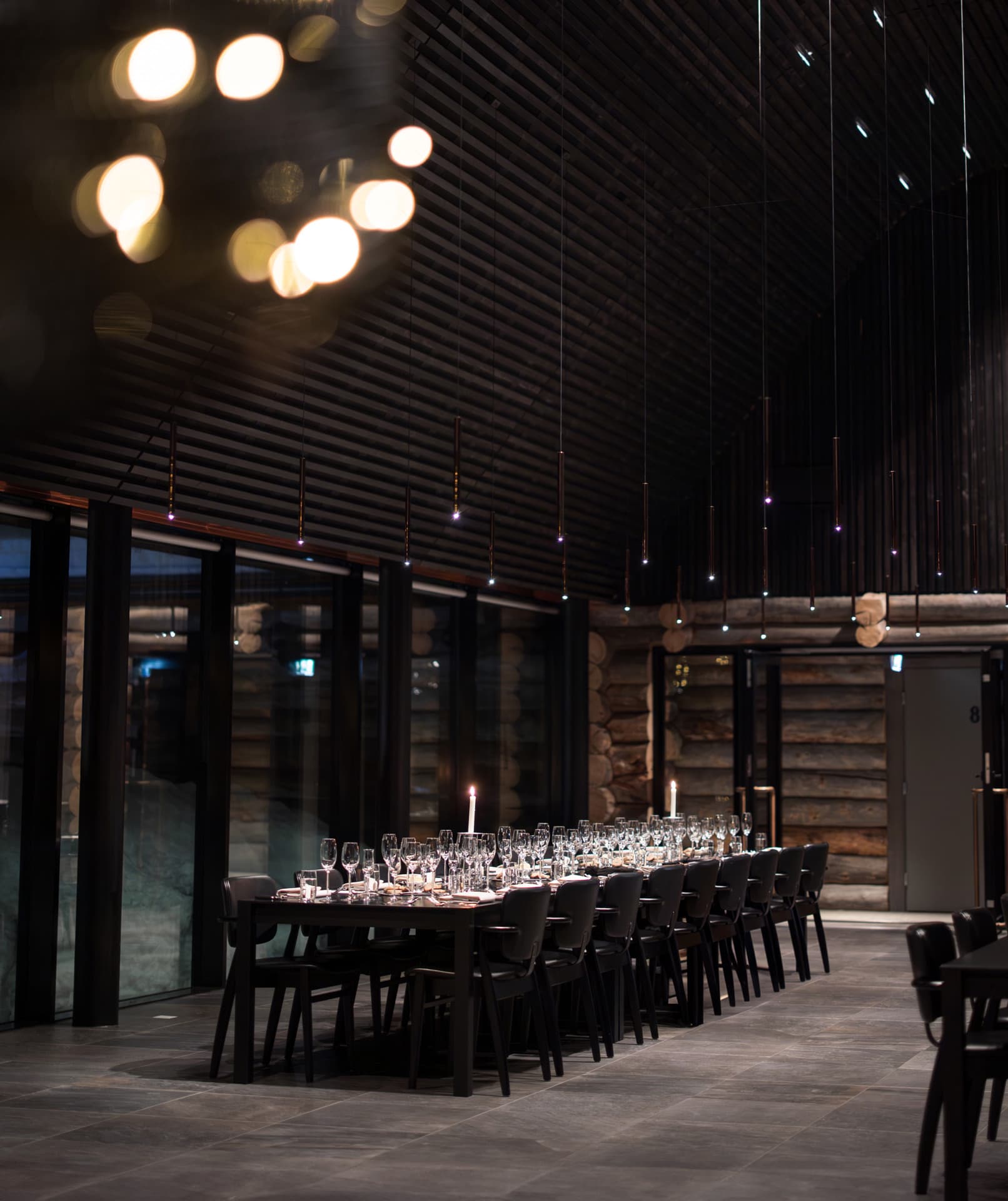 A long dining table beautifully set with glasses and plates in a dark, candlelit room at night.
