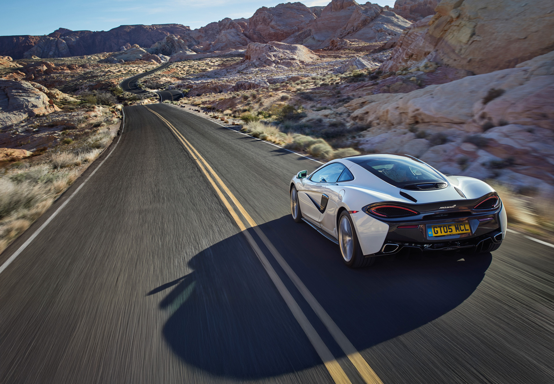 McLaren 570GT driving, at speed, down a rocky desert road.