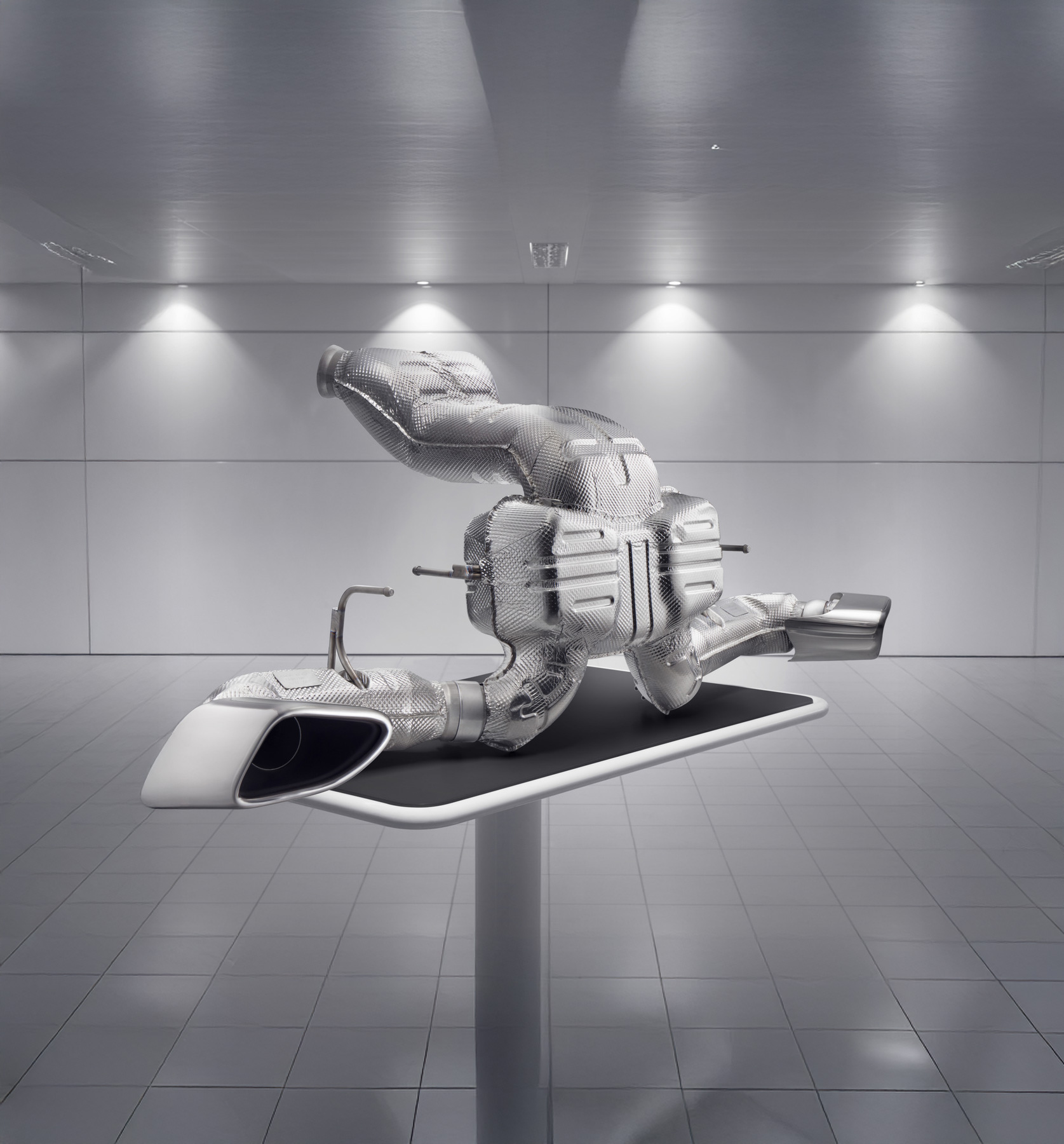 A detailed McLaren exhaust system displayed on a stand in a modern, clean showroom.