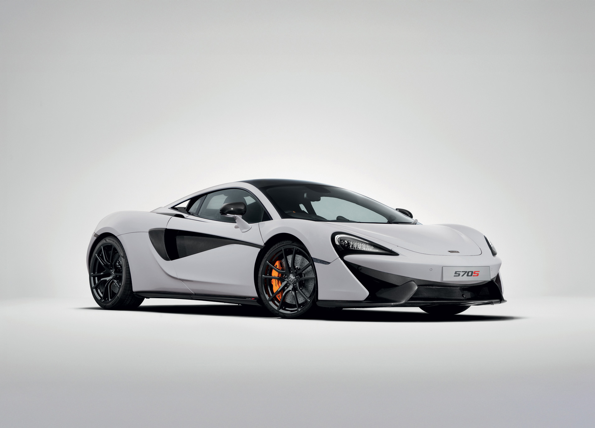 A white McLaren 570S sports car with orange brake calipers is shown from a front-three-quarter view on a white background.