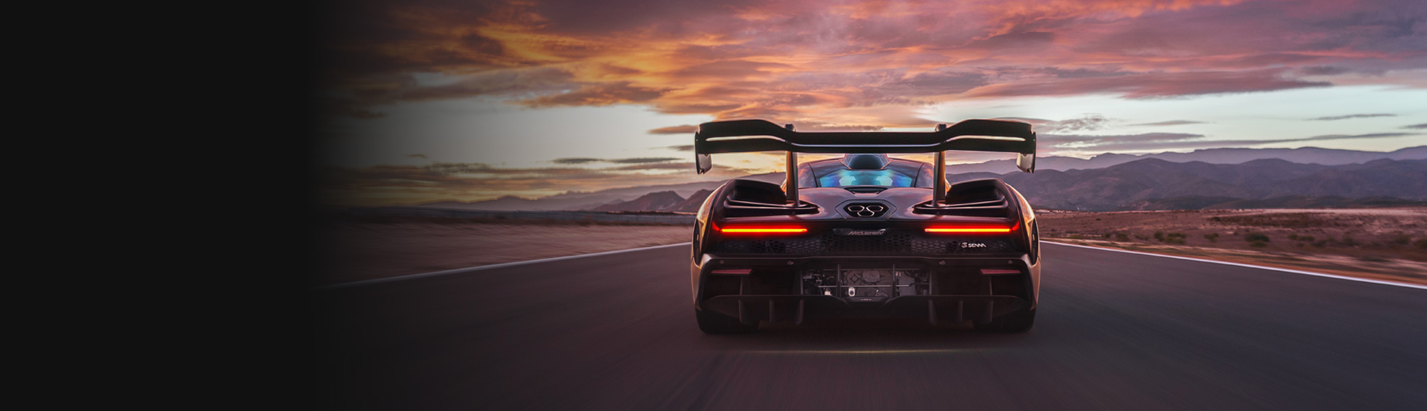McLaren Senna driving towards mountains at sunset.