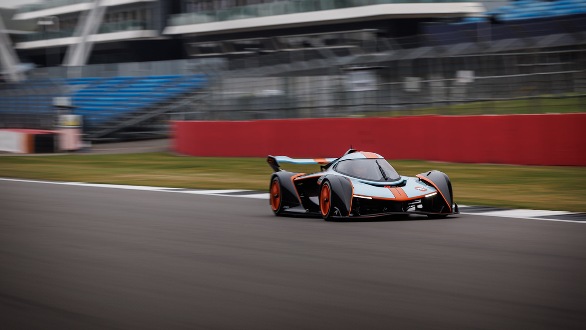 McLaren Solus GT track-only hypercar in the iconic Gulf racing livery (blue and orange) speeding on a professional racetrack. Dynamic shot capturing the speed and performance of the exclusive McLaren track experience car.