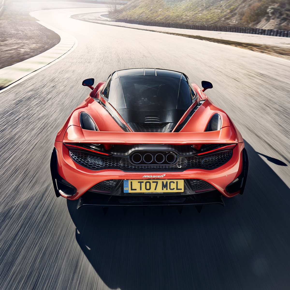 A top-down rear view of the red McLaren 765LT, a track-focused supercar, driving at speed on a circuit.