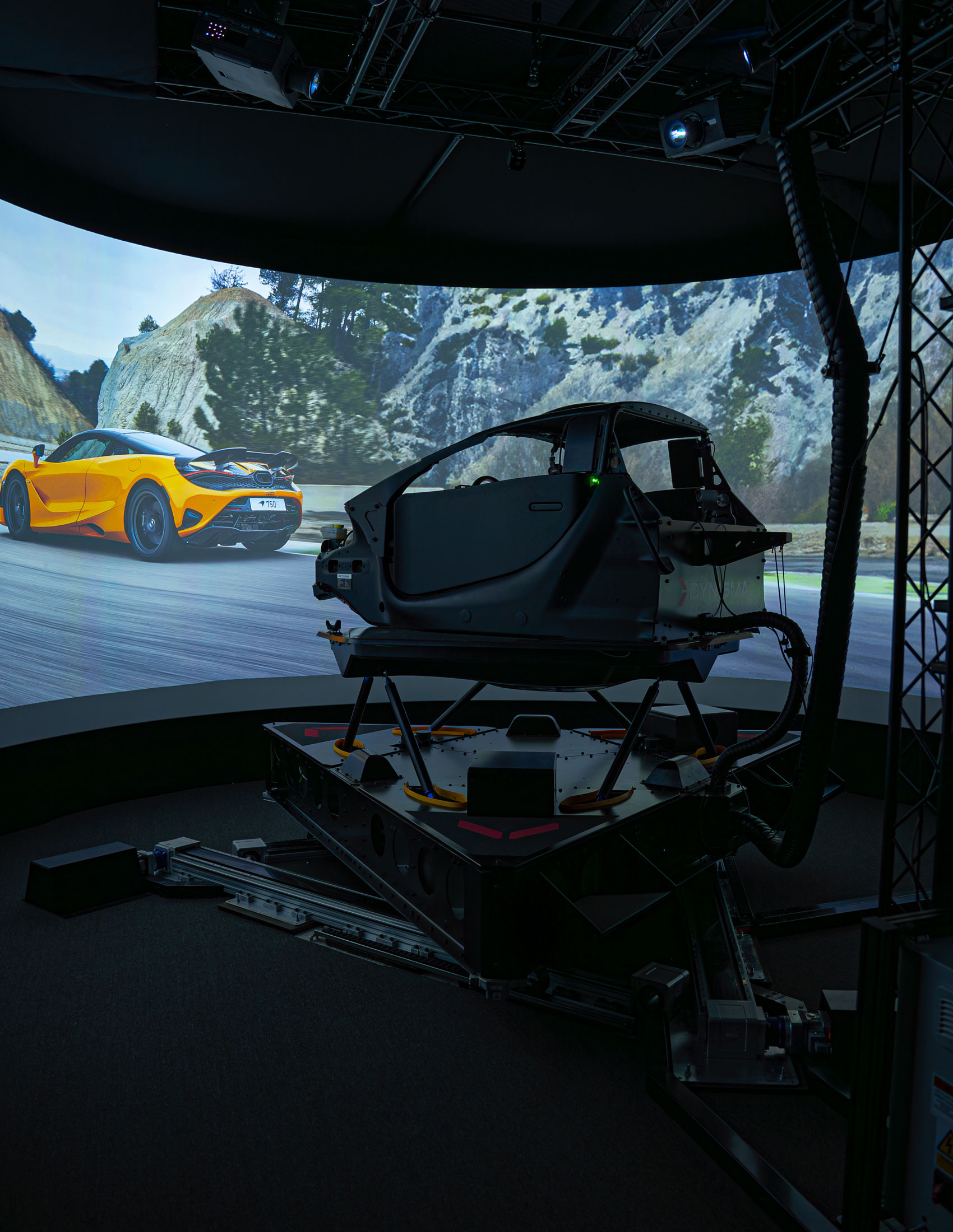 Dynisma automotive simulator surrounded by a screen which show an orange McLaren 750s driving on a mountain road.