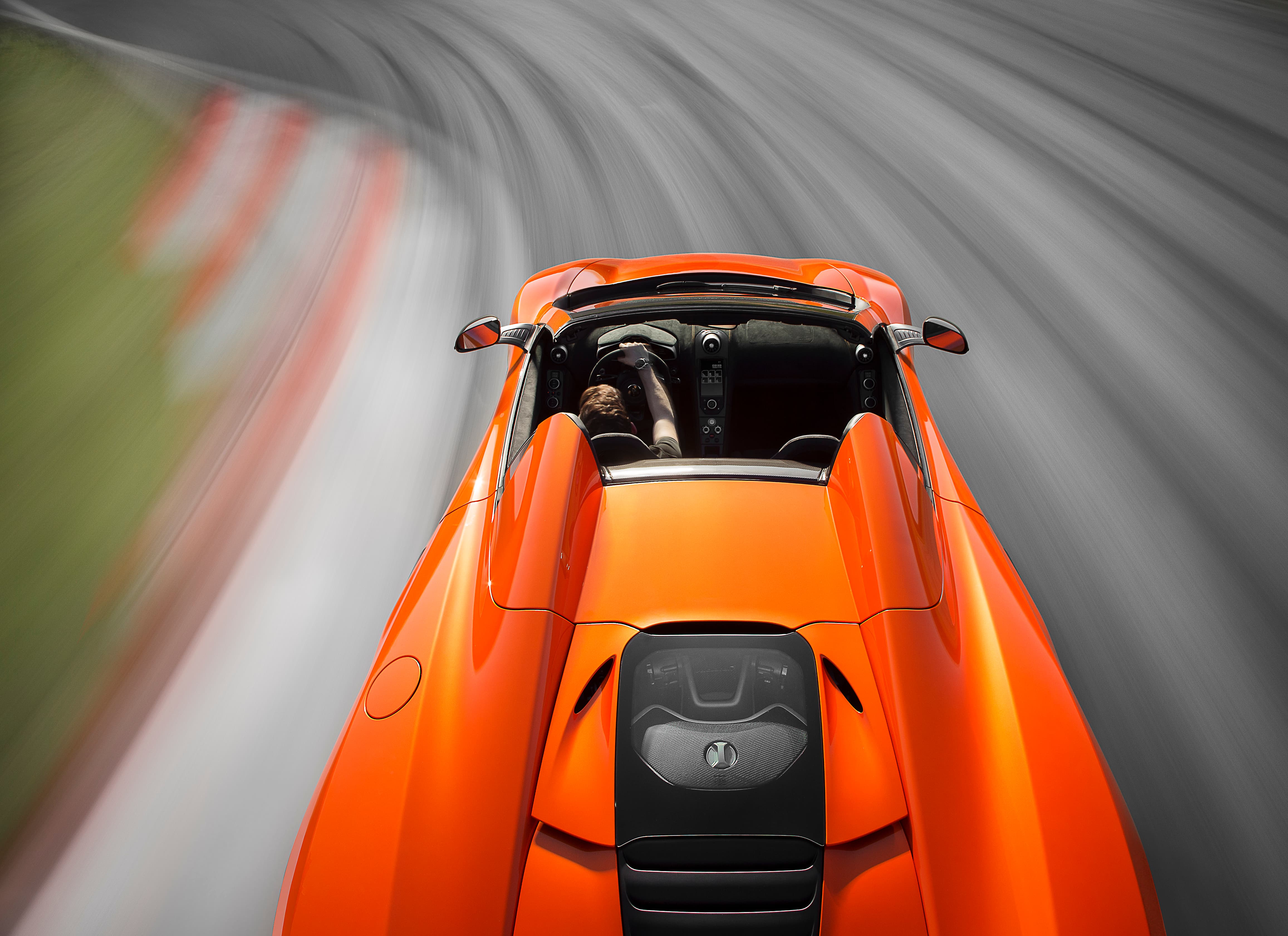 Rear view of an orange McLaren 650S Spider, photographed on a bright track environment.