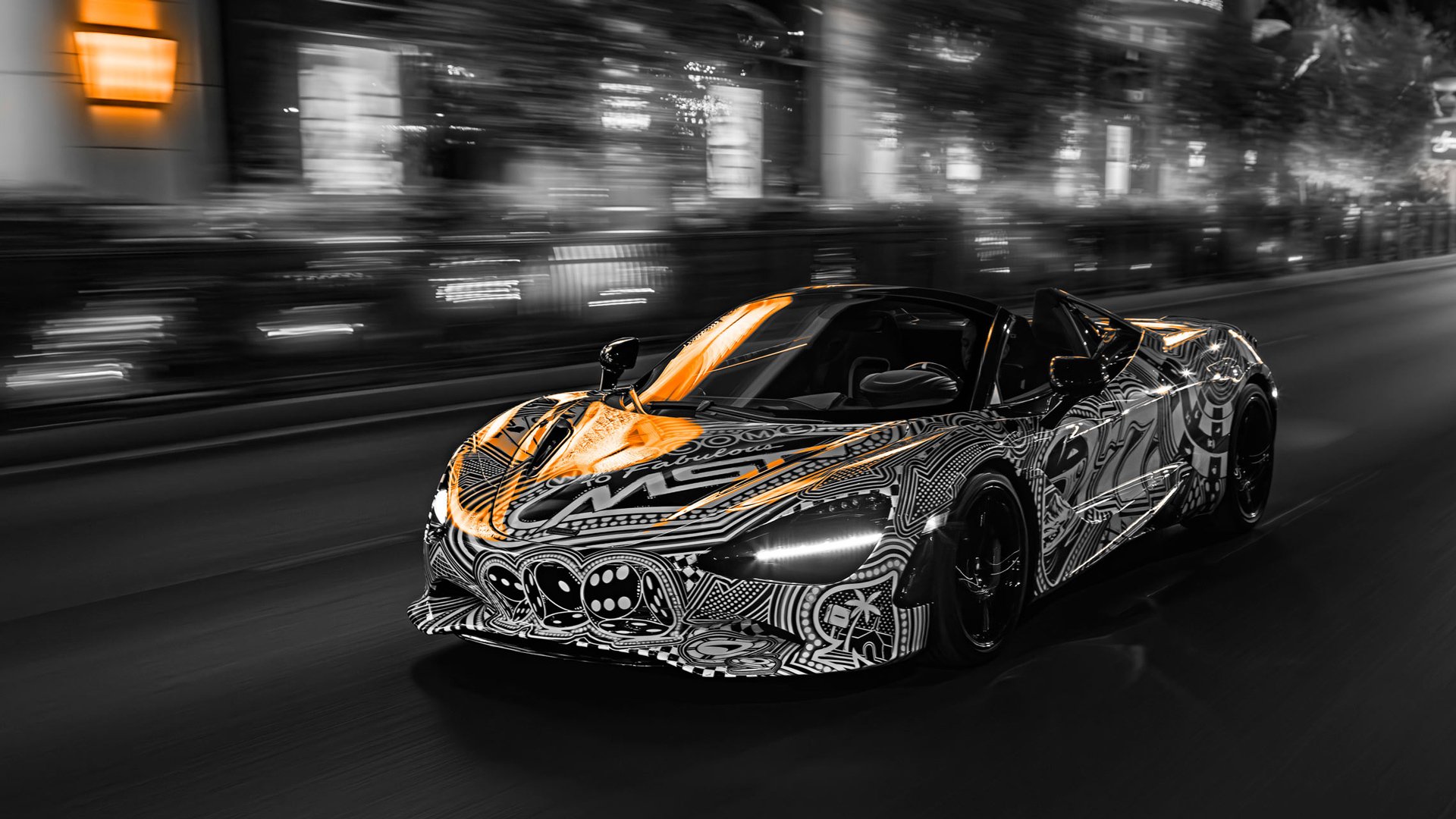 Motion blur shot of the McLaren 750S Spider 'Project Viva' speeding down a Las Vegas street at night, highlighting the black-and-white MSO livery with key elements selectively highlighted by McLaren orange lighting..