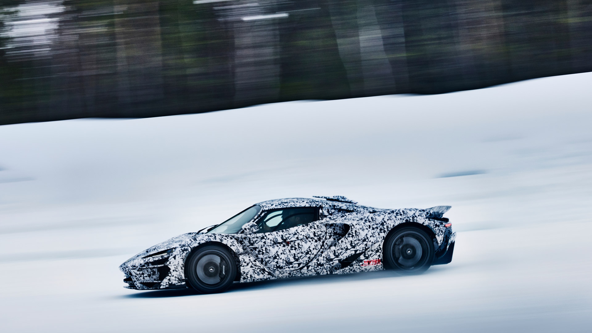 A camouflage-wrapped McLaren W1 prototype speeds across a snowy landscape, with blurred trees in the background, creating a sense of motion.